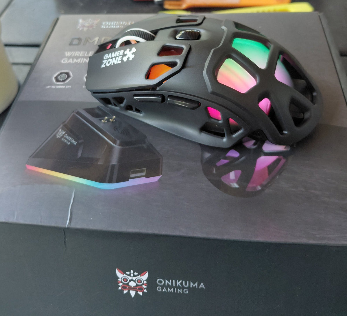 ONIKUMA DM09 wireless gaming mouse with RGB lighting on, resting beside its lit RGB charging dock