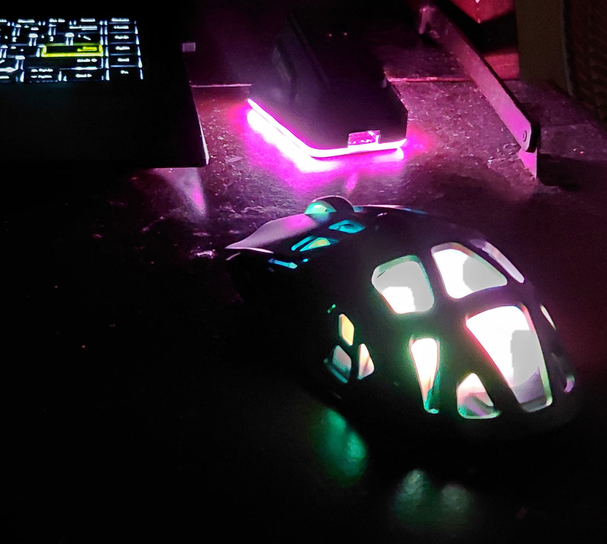 ONIKUMA DM09 gaming mouse glowing green and pink on a dark desk, RGB charging dock lit behind it